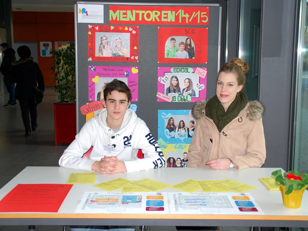 Zwei Jugendliche sitzen an einem Stand vor der Stellwand „Mentoren 14/15“.